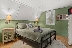 Un dormitorio con una cama individual, lámparas de noche, una mesita auxiliar pequeña, un aparador de madera y una ventana con persianas.