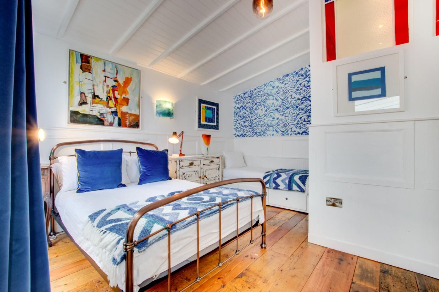 A bedroom with a bed, bedside table, lamp, and artwork on the wall.