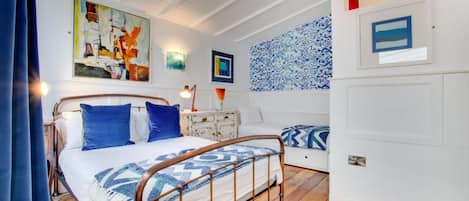 A bedroom with a bed, bedside table, lamp, and artwork on the wall.