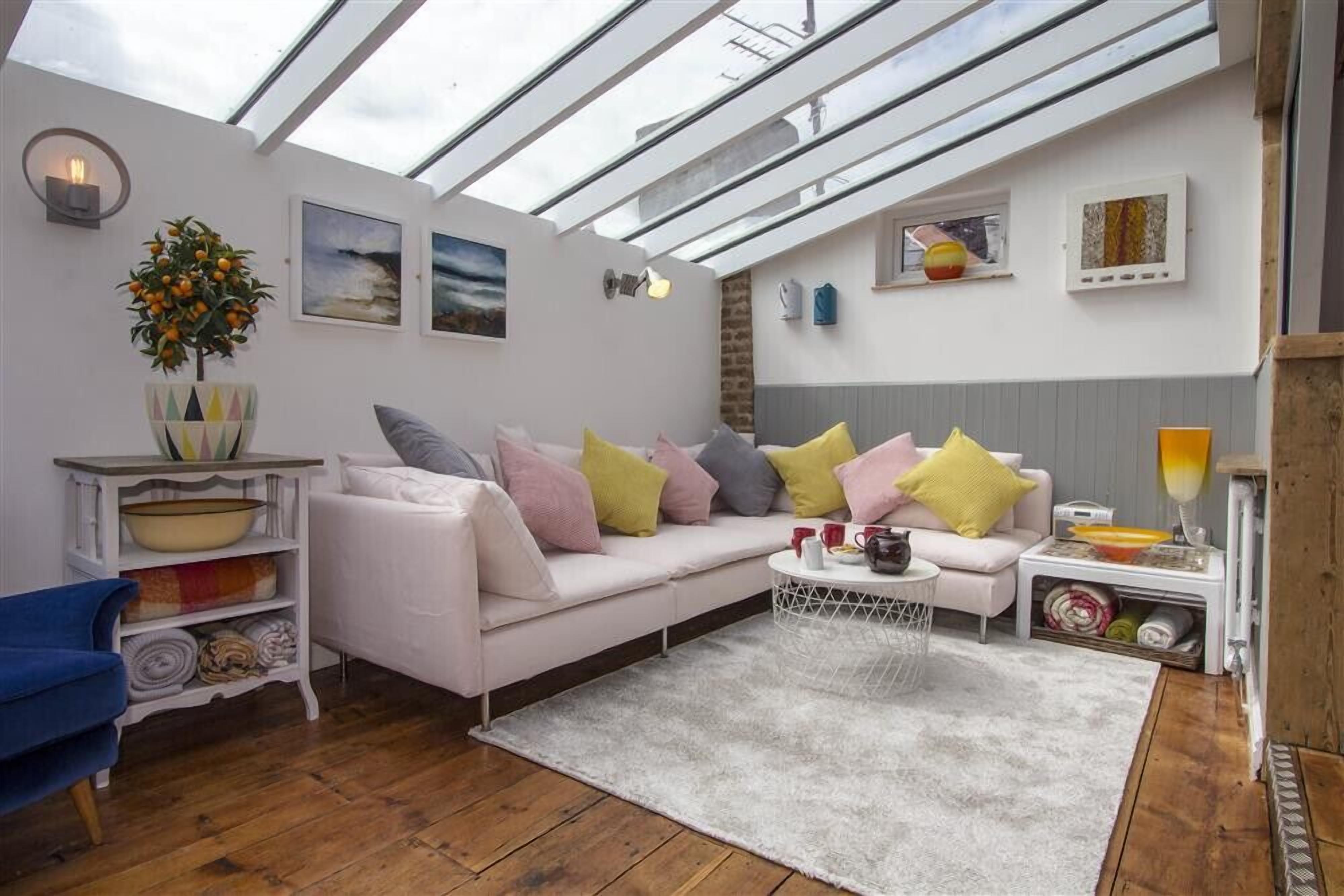 A modern living room with a white sofa, colorful cushions, a round coffee table, and a skylight above.