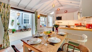 A dining area with a wooden table set for four, a kitchen with white cabinets, and a view of the outside patio. - 5 Bed in St. Ives (oc-baktre) (St Ives)