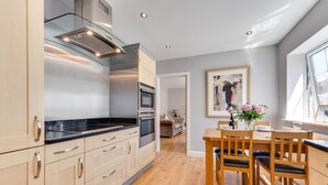 A modern kitchen with wooden cabinets, a black countertop, stainless steel appliances, and a dining area with a wooden table and chairs. - 2 Bed in Fowey (oc-jackda) (Fowey)