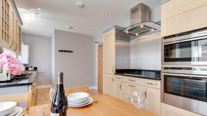 A modern kitchen with stainless steel appliances, wooden cabinets, and a dining area with a table set for two. - 2 Bed in Fowey (oc-jackda) (Fowey)