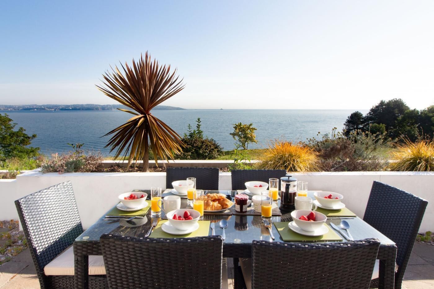 A dining table set with breakfast items and a view of the sea.
