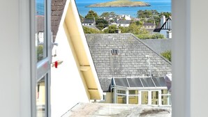 A dining area with a table set for two, overlooking a coastal town with houses and a view of the sea. - 4 Bed in Abersoch (oc-21tan) (Abersoch)