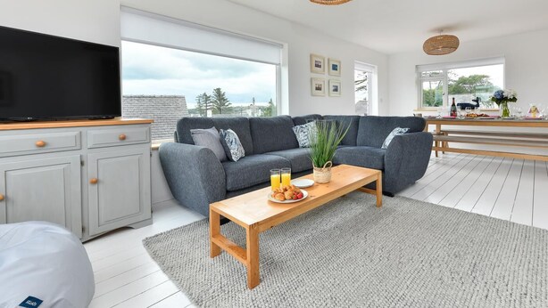 A modern living room with a grey sofa, wooden coffee table, and a flat-screen TV on a cabinet. - 4 Bed in Abersoch (oc-21tan) (Abersoch)