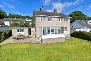 A two-story house with a conservatory, a patio with outdoor furniture, and a well-maintained lawn. - 3 Bed in Llanbedrog (oc-glensi) (Llanbedrog)