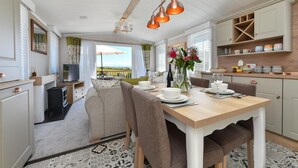 A modern kitchen with a dining area, featuring a large table set for four, a built-in oven, and a view of the outdoors. - 2 Bed in Abersoch (oc-atacam) (Abersoch)