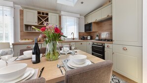 A modern kitchen with a dining table set for four, a vase of flowers, and a skylight above. - 2 Bed in Abersoch (oc-atacam) (Abersoch)