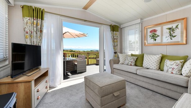 A cozy living room with a television, sofa, and ottoman, a balcony with outdoor furniture, and a scenic view. - 2 Bed in Abersoch (oc-atacam) (Abersoch)