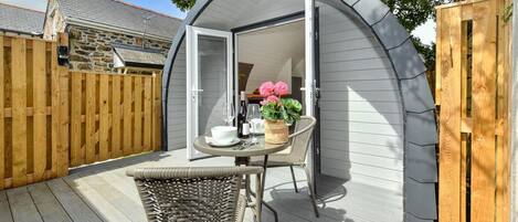 Un espace extérieur abrité, avec une table et des chaises, une clôture en bois et un bâtiment en pierre en arrière-plan.