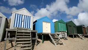 Une rangée de cabanes de plage, avec des escaliers en bois menant à chacune d’elles, installées sur une plage de sable.