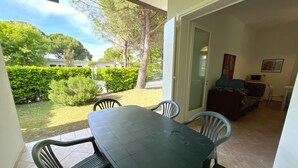 A patio area with a table and chairs, a sofa, and a door leading to a garden. - VILLA DOGI NORTH - A2 6+0 - B80F15 (Bibione Pineda)