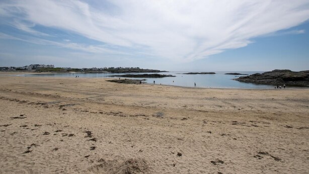 A wide sandy beach with calm water, rocky outcrops, and distant buildings. - 2 Bed in Talwrn (oc-wai228) (Ysgubor Hen)
