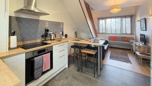 A modern kitchen with a central island, a dining area with a wooden table and bar stools, and a living room with a sofa and TV. - 2 Bed in Talwrn (oc-wai228) (Ysgubor Hen)