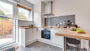 A modern kitchen with white cabinets, a built-in oven, a coffee machine, and a patterned backsplash. - 2 Bed in Talwrn (oc-wai228) (Ysgubor Hen)