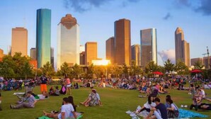 Ein Park mit Menschen, die im Gras entspannen, umgeben von einer Stadtlandschaft mit hohen Gebäuden.