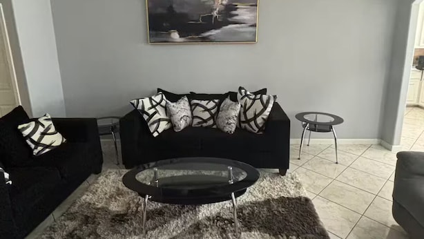 Ein Wohnzimmer mit einer schwarzen Couch, einem Glastisch und einem Gemälde an der Wand.