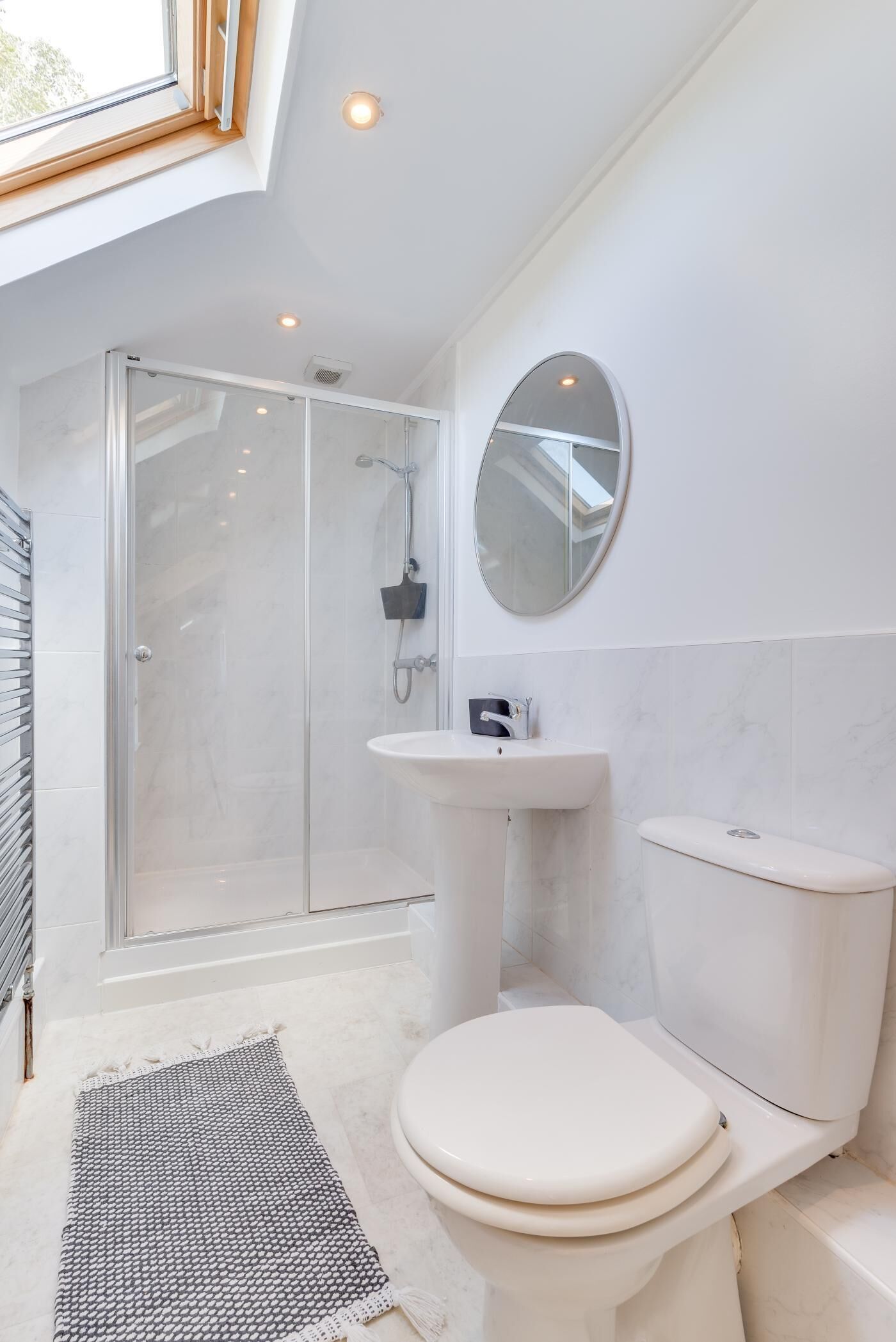 A modern bathroom with a glass shower enclosure, a pedestal sink, a toilet, and a skylight above.