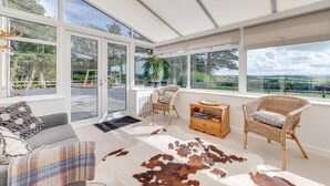 Una habitación amplia con ventanas grandes, un tapiz de cuero de vaca, muebles de mimbre y vistas al campo.