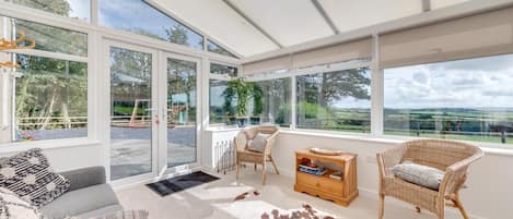 Una habitación amplia con ventanas grandes, un tapiz de cuero de vaca, muebles de mimbre y vistas al campo.
