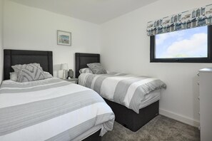 Une chambre avec deux lits, une table de chevet, une lampe, un tableau au mur et une fenêtre avec un rideau.