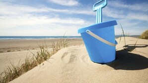 A blue bucket with a key-shaped handle on a sandy beach with the ocean in the background. - 2 Bed in Abererch (oc-glwysf) (Abererch)