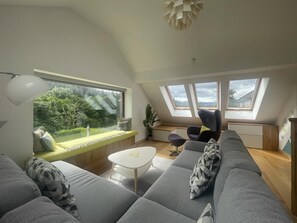Ein modernes Wohnzimmer mit großem Fenster, einer Couch, einem Couchtisch und einem Oberlicht.