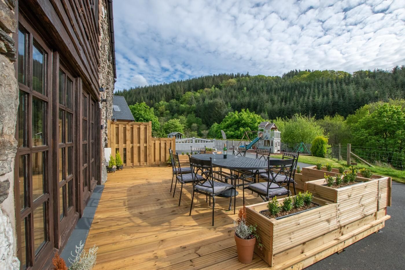A wooden deck with a table and chairs, surrounded by raised garden beds with plants.