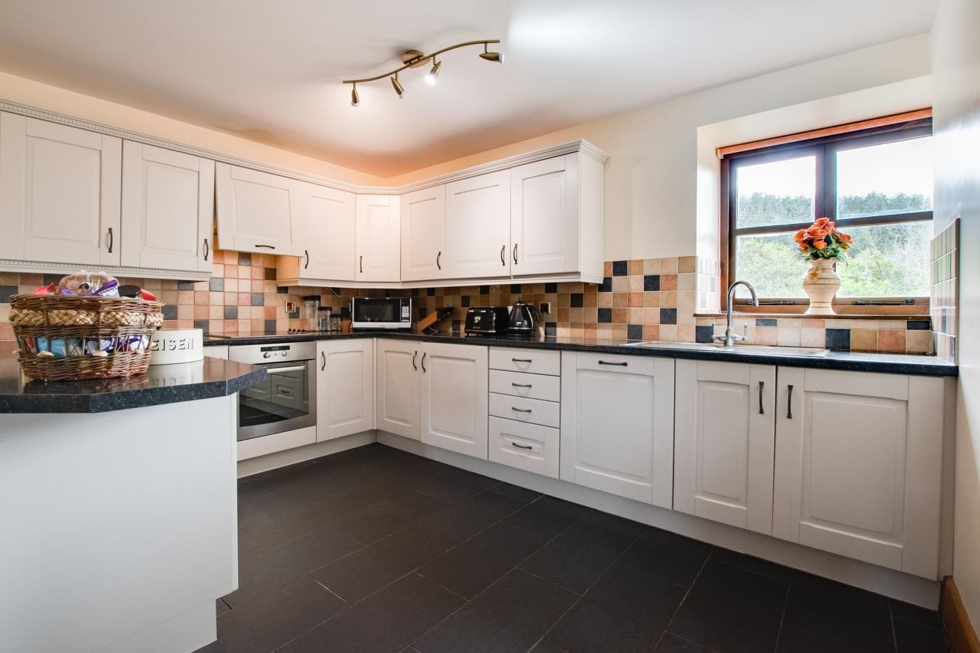 A modern kitchen with white cabinets, a microwave, a stove, and a window with a view.