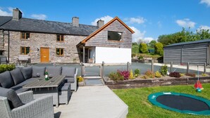 A stone house with a wooden extension, a patio with outdoor furniture, and a trampoline. - 6 Bed in Machynlleth (oc-bow374) (Glantwymyn)