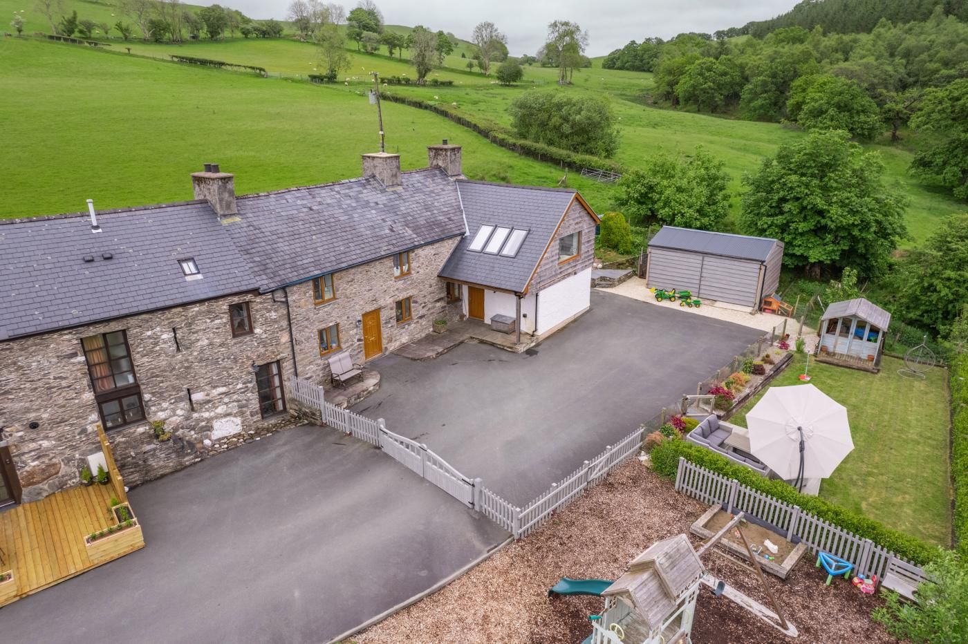 A stone farmhouse with a paved driveway, a small garden, and a barn.