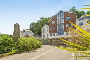 A modern building with a mix of brick and glass facades, a stone monument, and a road with greenery on the side. - 1 Bed in Fowey (oc-saila) (Fowey)