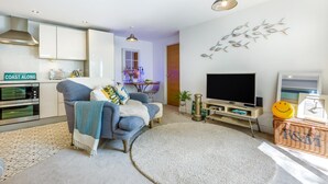 Een moderne woonkamer met een bank, een flatscreen televisie, een open haard en een keuken met een oven.