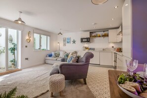 A modern living room with a sofa, ottoman, and a dining table with a salad. - 1 Bed in Fowey (oc-saila) (Fowey)
