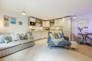 A modern living room with a sofa, a blue armchair, and a dining area with a table and chairs. - 1 Bed in Fowey (oc-saila) (Fowey)