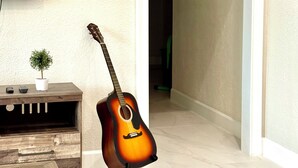 Ein Zimmer mit einer an der Wand angelehnten Gitarre, einem an einer Holzkonsole montierten Fernseher und einem Blumentopf auf der Konsole.