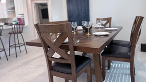 Ein Essbereich mit Holztisch und -stühlen, im Hintergrund eine Küche und ein blauer Vorhang an der Wand.