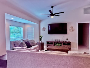 A living room with a sofa, a coffee table, a TV, and a ceiling fan. - Westport Reserve Vacation Home w/ Private Pool | Family Friendly (Naples)