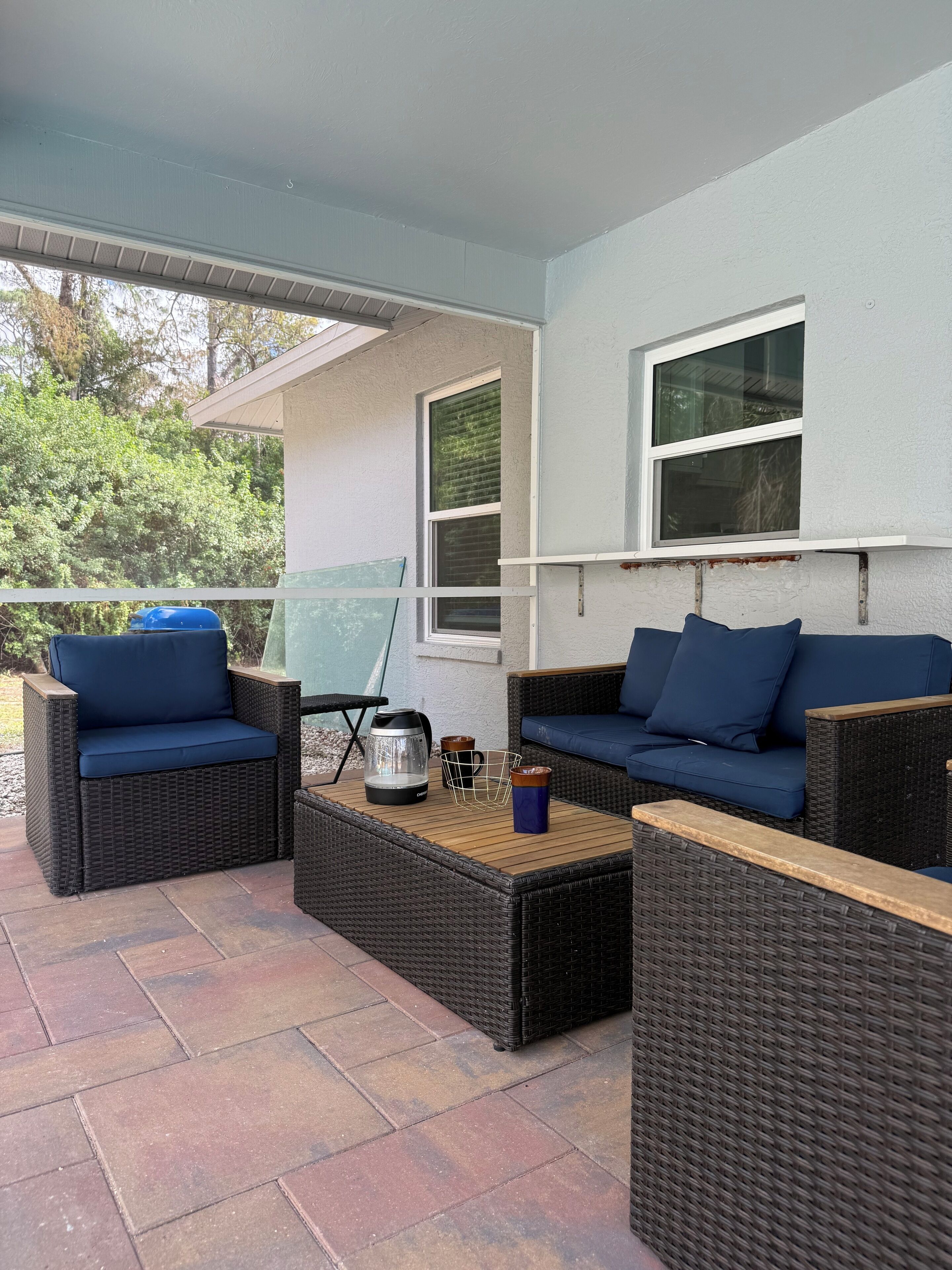 An outdoor patio area with wicker furniture, including two sofas and a coffee table, and a glass door leading to a garden.
