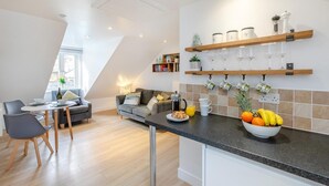 A modern kitchen with a breakfast bar, a dining area with a sofa and chairs, and a kitchen island with fruit and a coffee maker. - 1 Bed in St. Ives (oc-h27240) (St Ives)