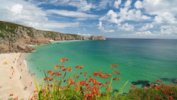 A coastal beach with clear turquoise waters, rocky cliffs, and red flowers in the foreground. - 1 Bed in St. Ives (oc-h27240) (St Ives)