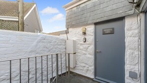 A white exterior wall with a grey door, a small white electrical box, and a metal railing. - 1 Bed in St. Ives (oc-h27240) (St Ives)