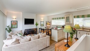 Un salon moderne comprenant un canapé, un téléviseur à écran plat, une cheminée et un coin repas avec une table et des chaises.