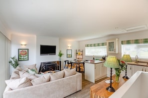A modern living room with a sofa, a flat-screen TV, a fireplace, and a dining area with a table and chairs. - 2 Bed in Abersoch (oc-s27221) (Abersoch)