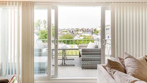 Un salon comprenant un canapé, une table à manger avec des chaises et une porte-fenêtre coulissante donnant sur une terrasse extérieure avec un canapé en osier et une table.
