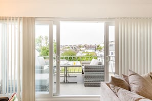 A living room with a sofa, a dining table with chairs, and a sliding glass door leading to an outdoor patio with a wicker sofa and a table. - 2 Bed in Abersoch (oc-s27221) (Abersoch)