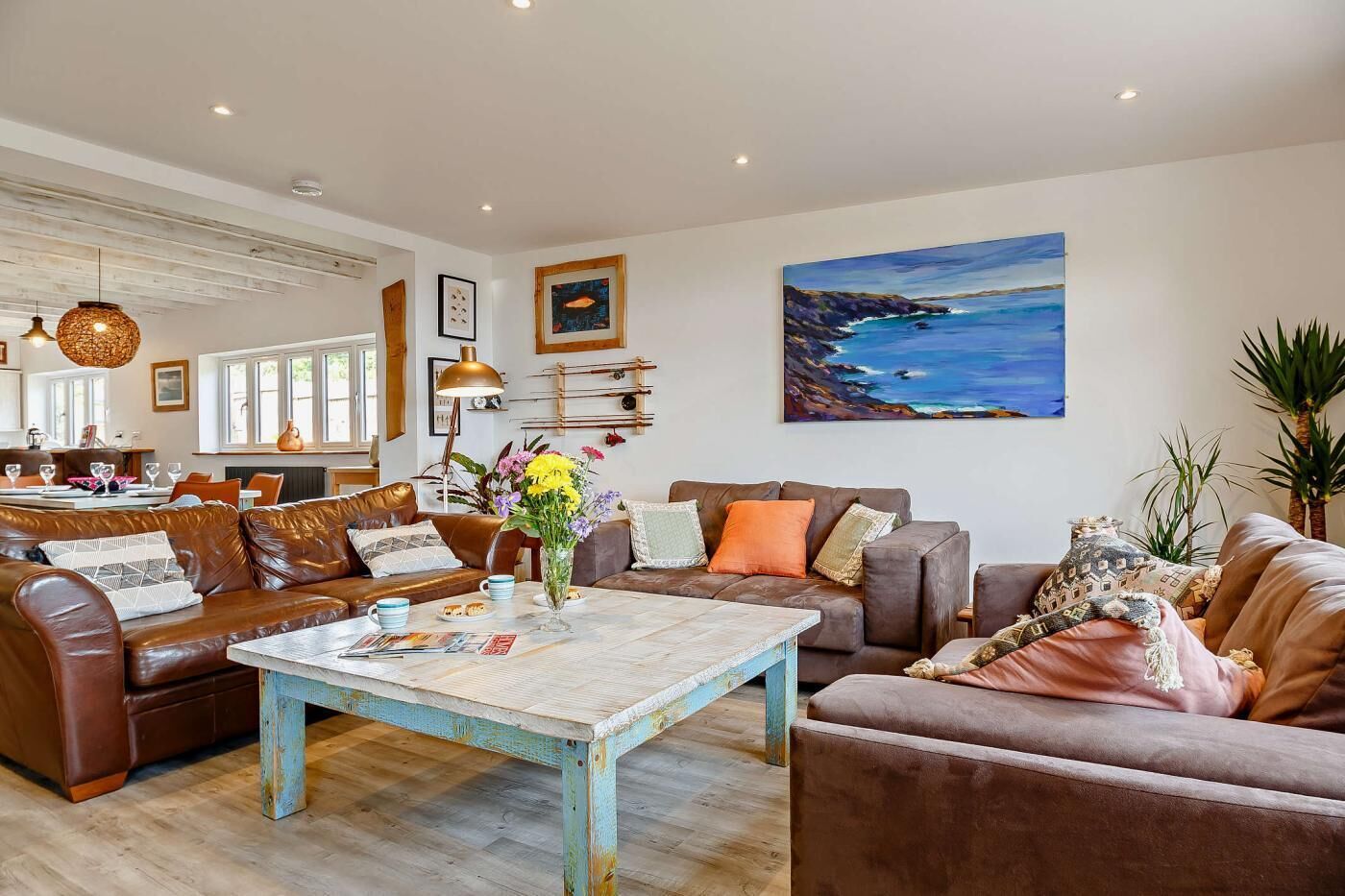 A spacious living room with a brown leather sofa, a coffee table, and a painting of a coastal landscape.