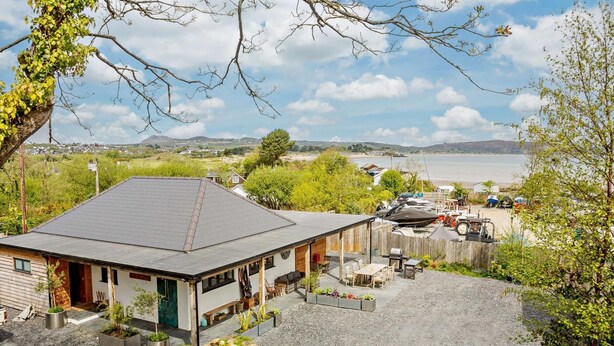 Et hus med skråt tag, overdækket terrasse og grusvej.