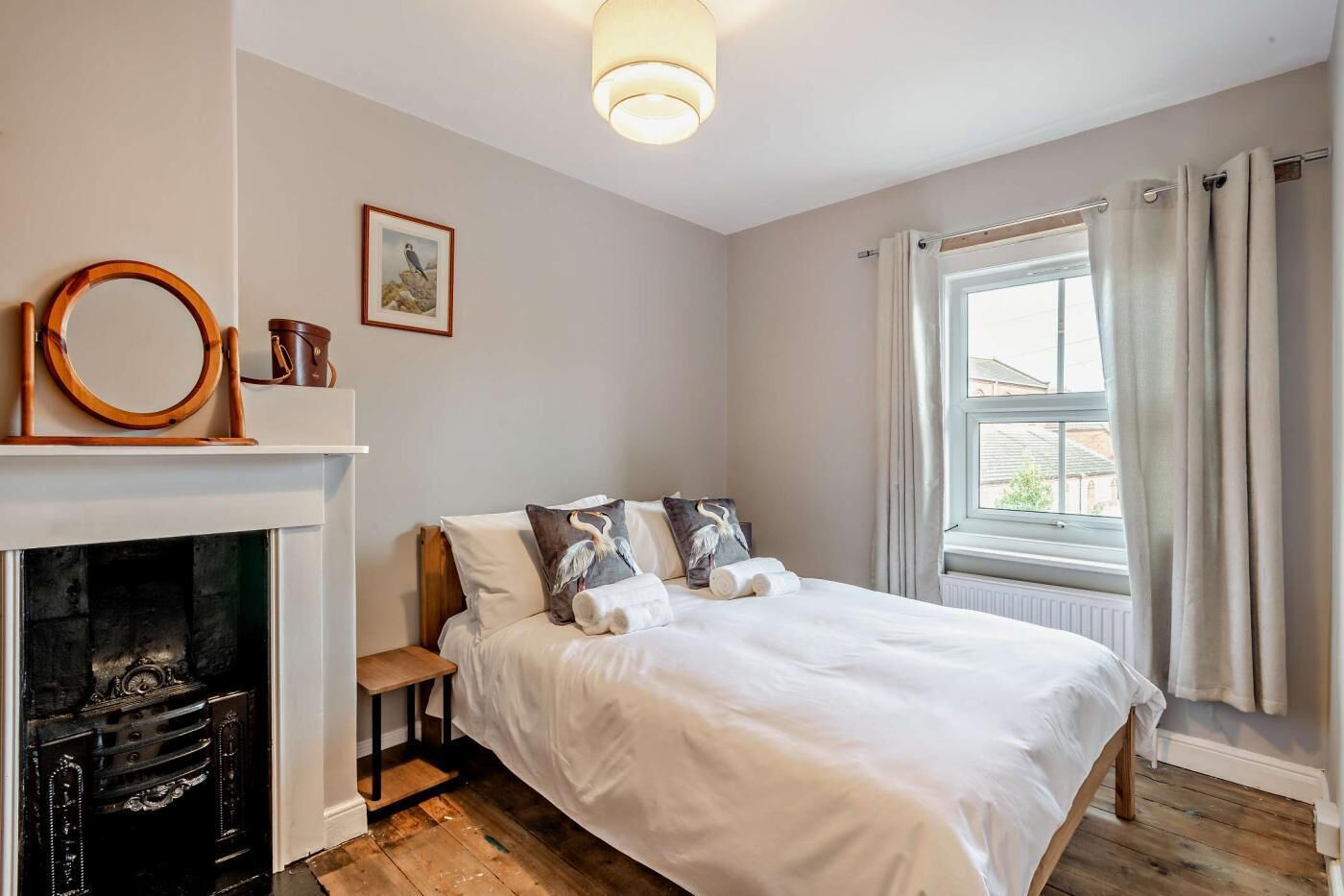 Une chambre à coucher avec un lit, une cheminée, une fenêtre avec des rideaux et un tableau accroché au mur.